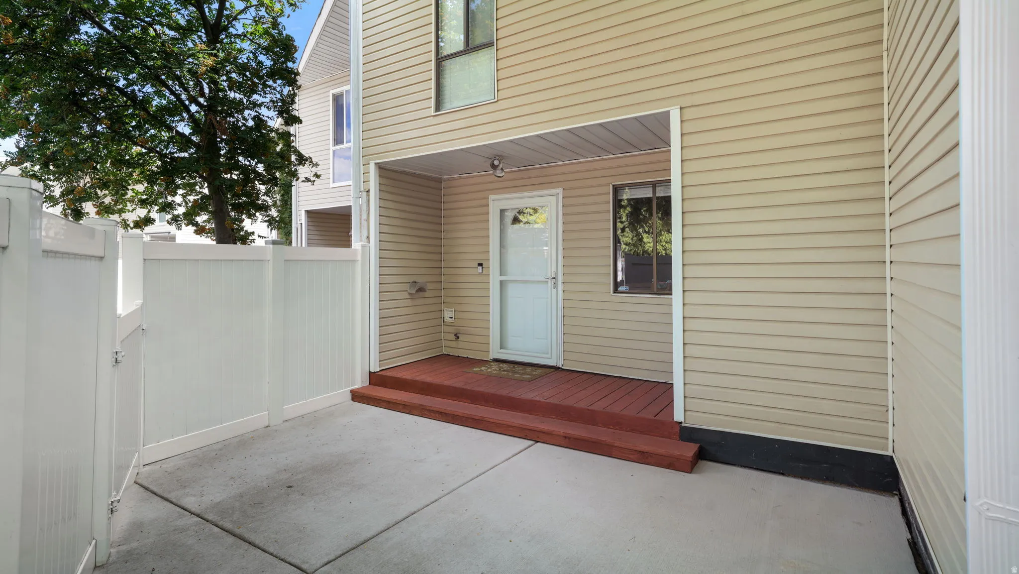 Private concrete patio area featuring a white vinyl fence and gate