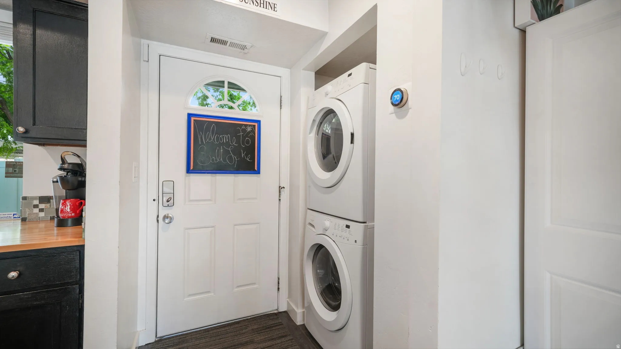 Entryway featuring a white paneled door with an arched window, wood-finish flooring, a stacked washer and dryer, and a smart thermostat