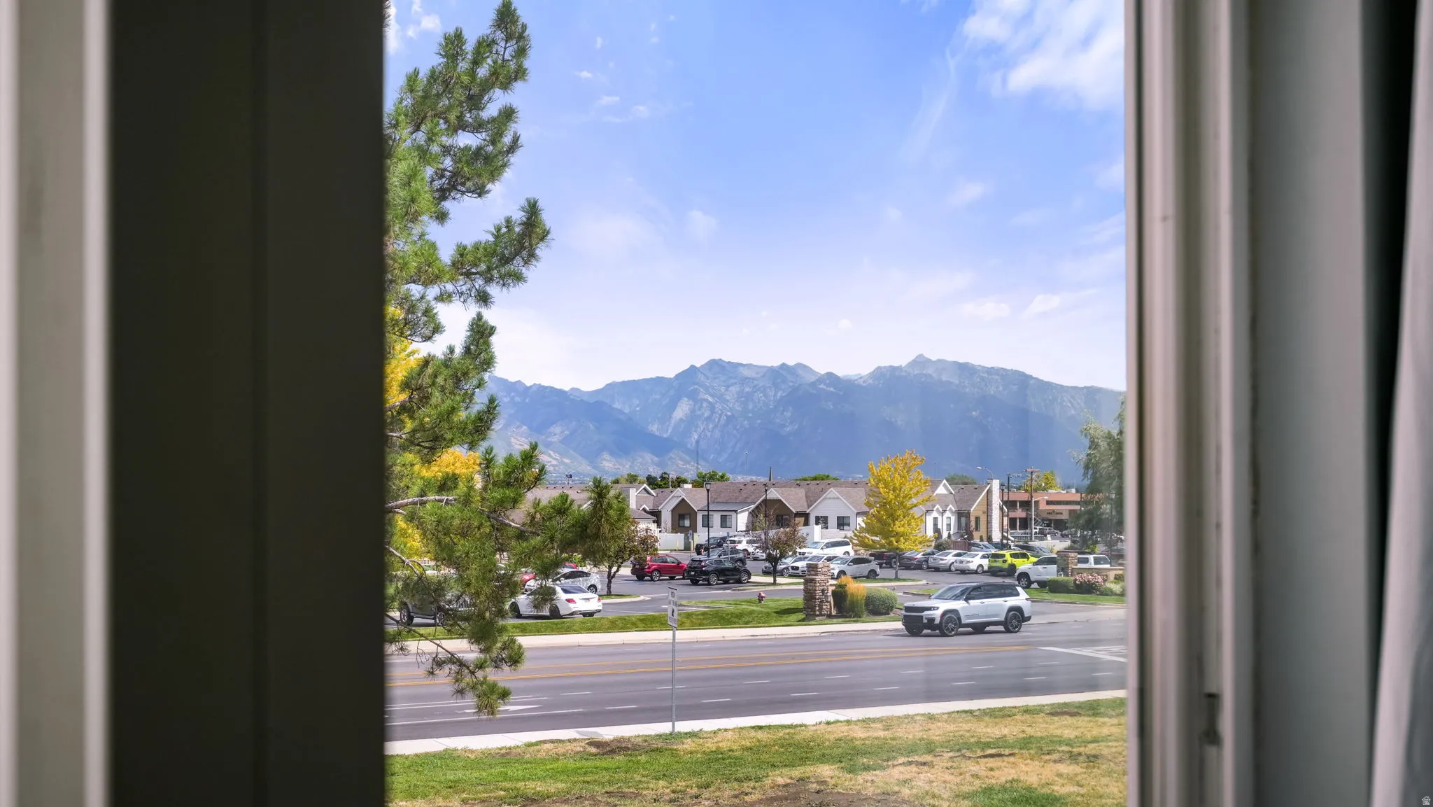 Mountainous backdrop visible through a window frame, with residential structures and a road in the foreground