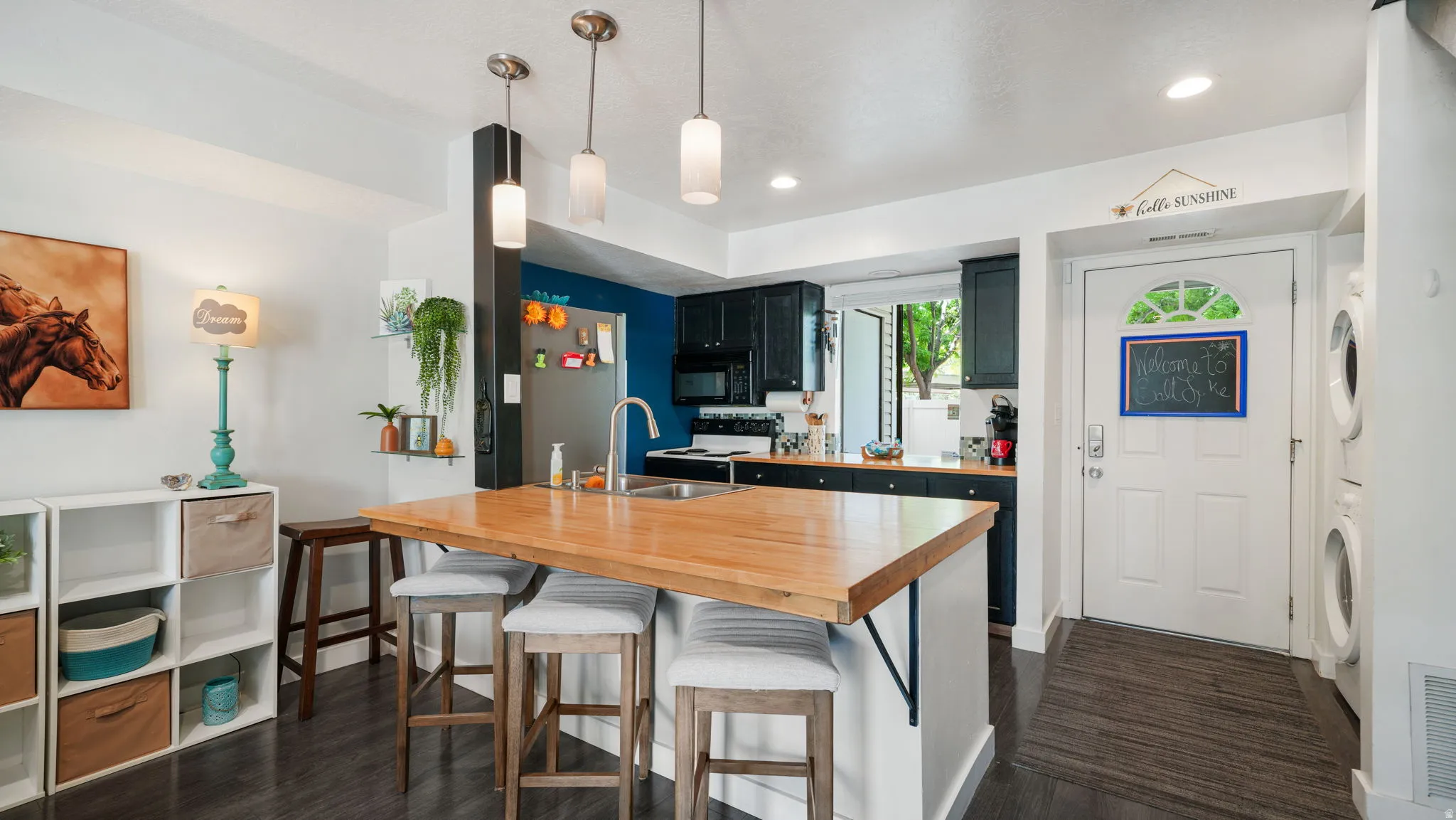 Kitchen featuring dark cabinetry, a natural wood-finish island with pendant lighting, and a stainless steel sink