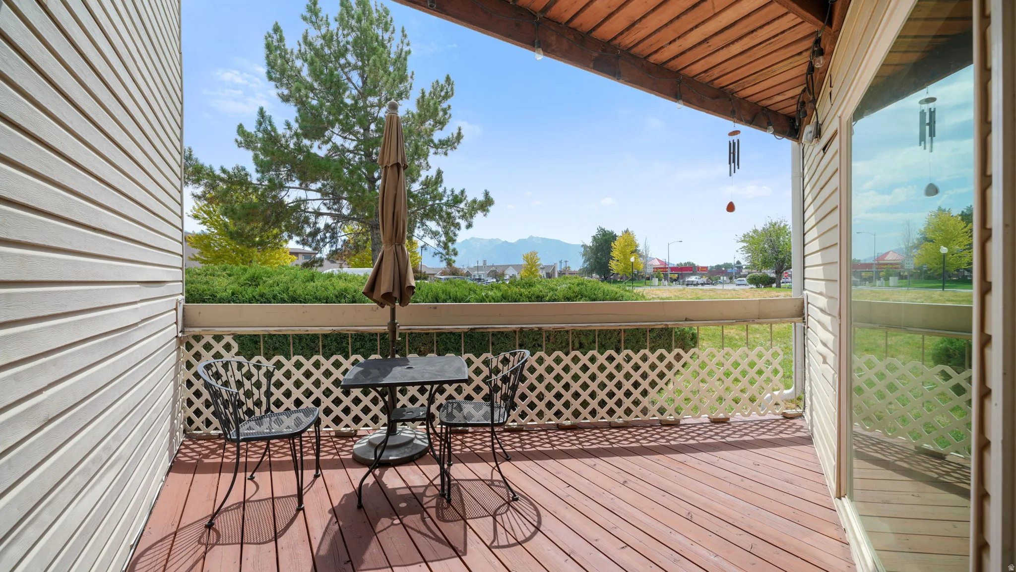 Covered wooden deck with slatted flooring, white lattice railing, and a sliding glass door