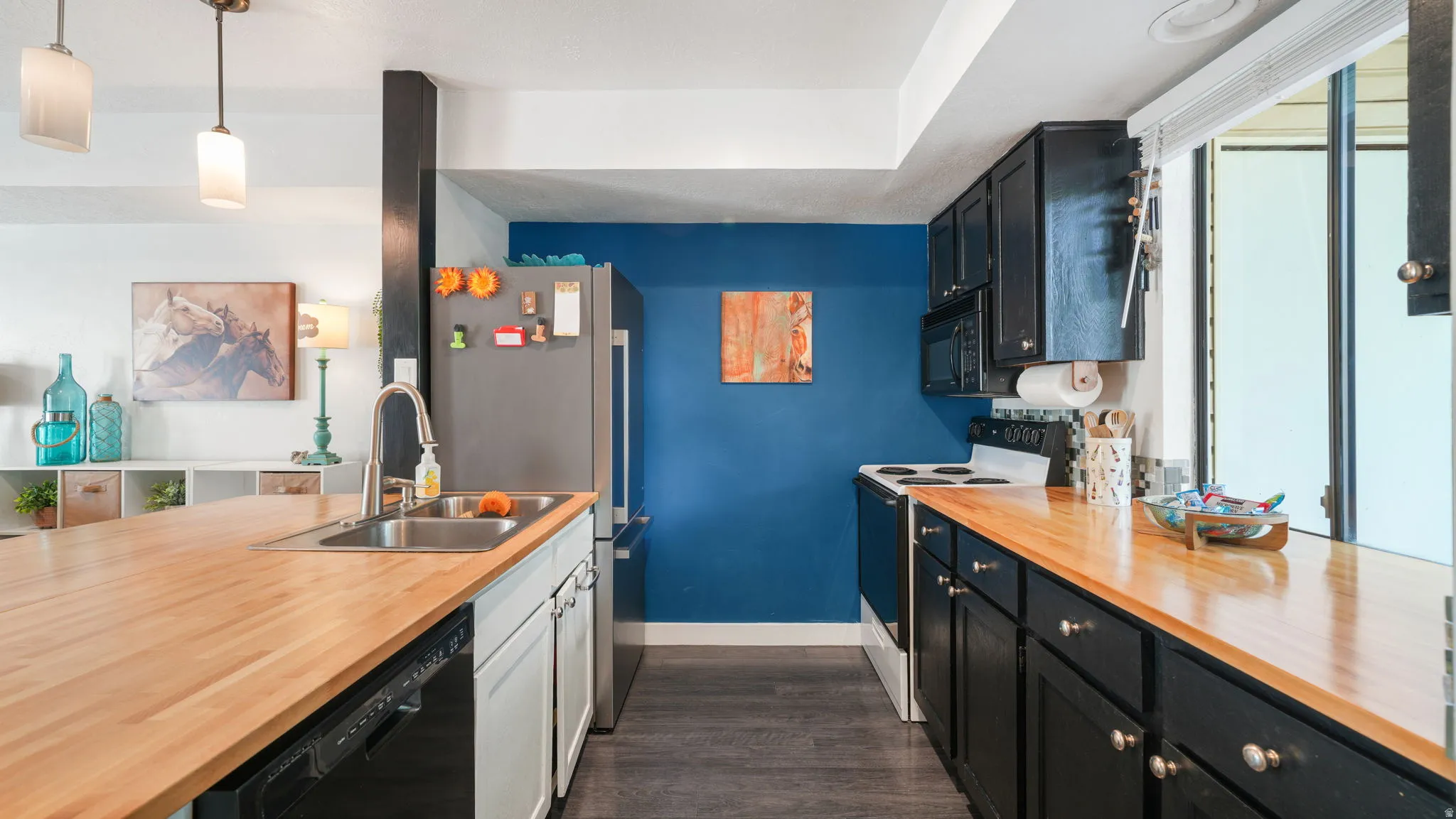 Kitchen featuring wood-finish countertops, stainless steel sink, black cabinetry with contrasting hardware, and a built-in dishwasher