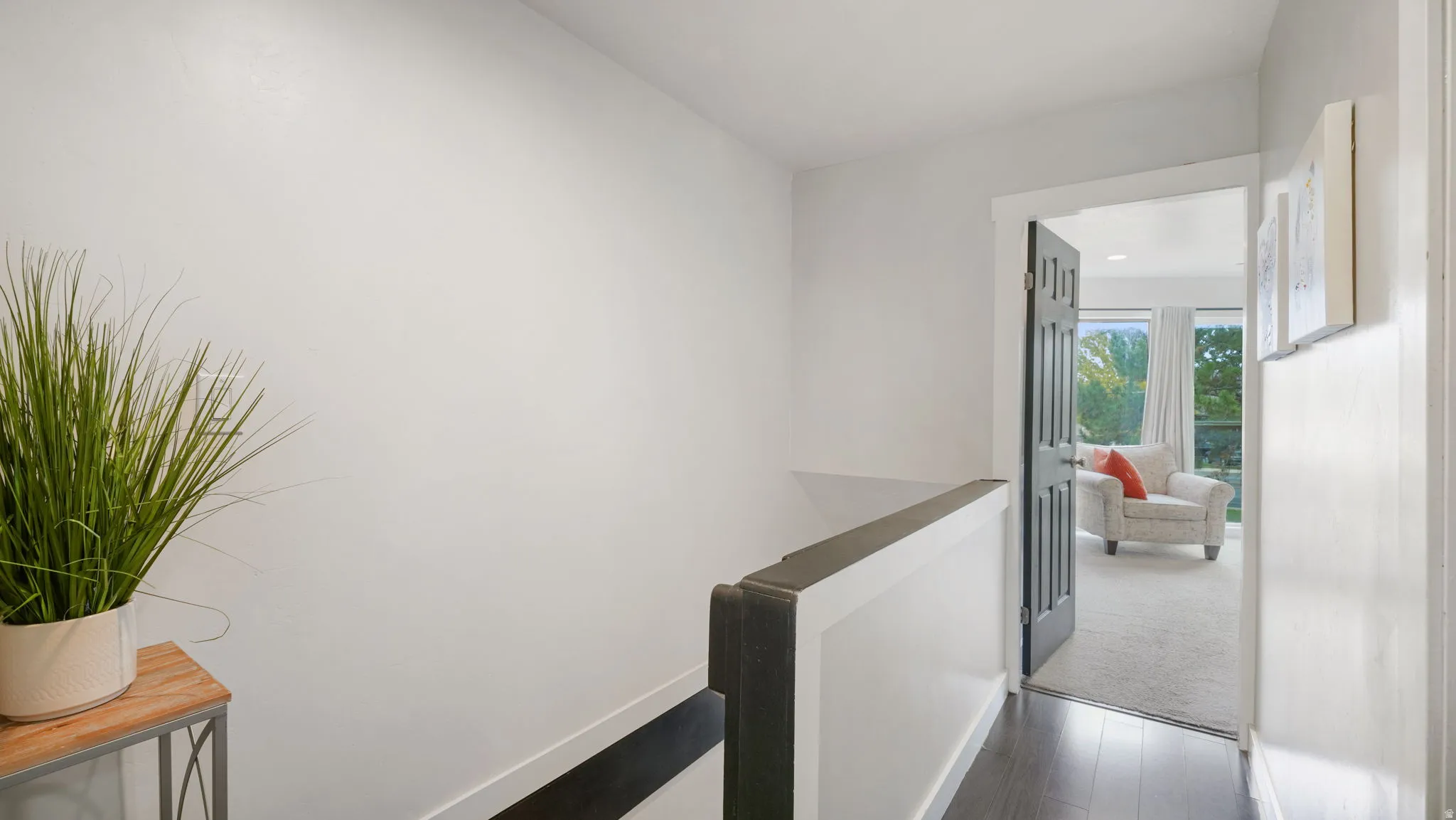 Hallway featuring dark wood-finish flooring, white walls, and a dark wood handrail