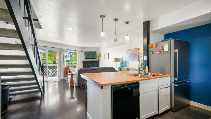 Open-concept living area featuring wood-finish flooring, a kitchen island with a double basin sink, white cabinetry, and a black dishwasher