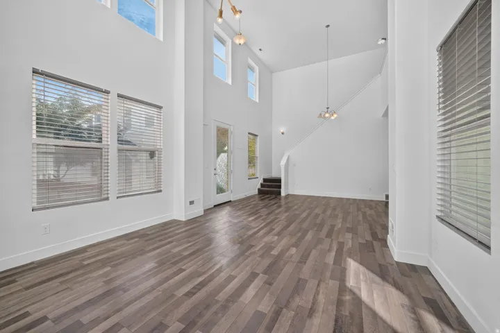 High ceilings, wood-finish flooring, multiple windows with blinds, a prominent staircase, and contemporary lighting fixtures