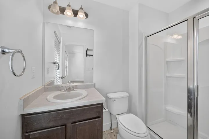 Vanity with integrated sink, rectangular mirror, three-light fixture, glass-enclosed shower, and toilet