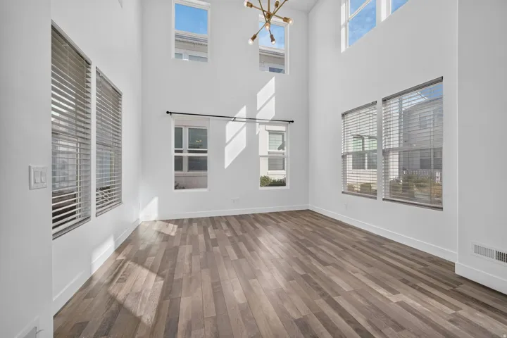 Two-story living space featuring a high ceiling, multiple windows, wood-finish flooring, and a modern chandelier