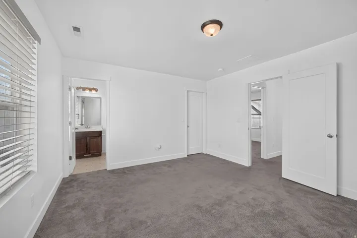 Spacious room with gray carpeting and white walls, featuring a window with blinds, a ceiling-mounted light fixture, and two white panel doors