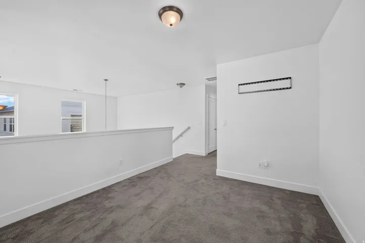 Carpeted landing area featuring a white railing, overhead lighting, and white walls