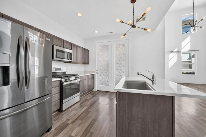 Stainless steel appliance package, wood-finish flooring, white countertops, built-in recessed lighting, and a contemporary chandelier