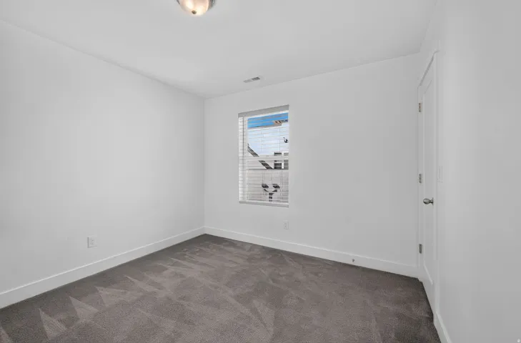 Neutral wall color, grey carpeting, window with blinds, overhead light fixture, white trim