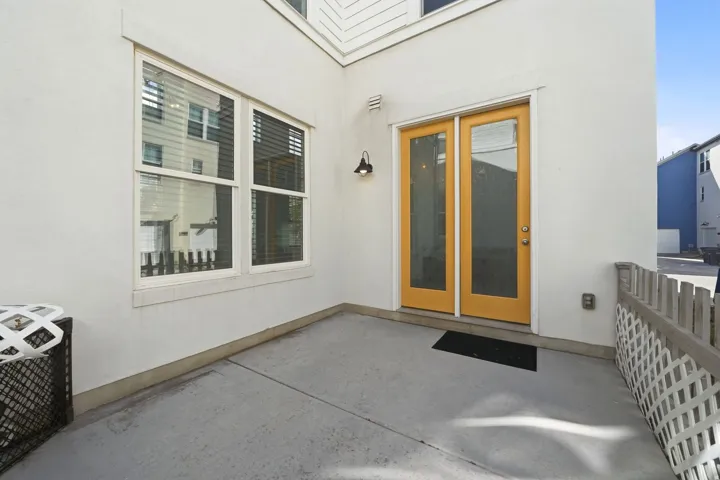 Private outdoor patio with a concrete surface, white stucco exterior, and a pair of yellow-framed glass panel doors