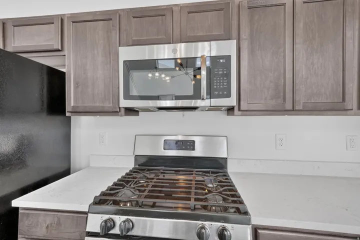 Stainless steel range with gas burners, stainless steel built-in microwave, wood-finish cabinetry, and solid surface countertops