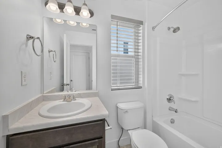 White bathroom featuring a single vanity with an integrated sink, a white toilet, and a white bathtub with an integrated shower