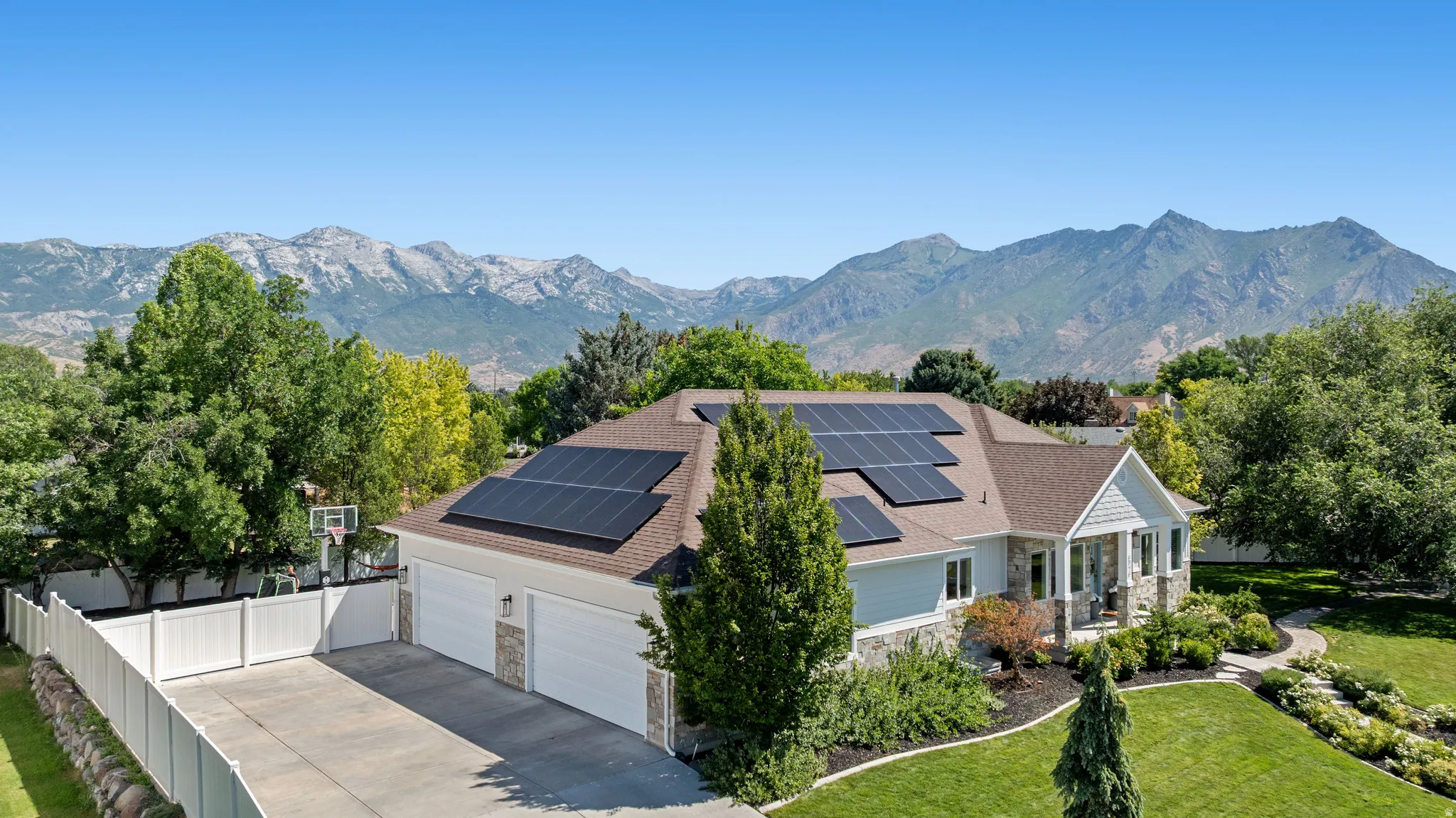Ranch-style residence featuring a stone and siding exterior, integrated solar panels, a four-car garage, and established landscaping