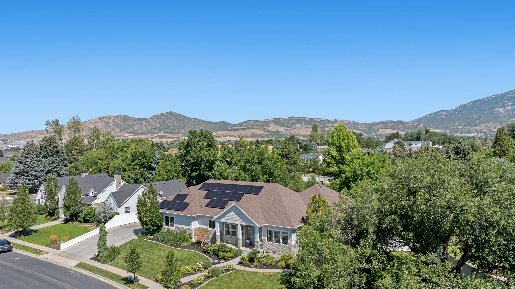Single-story residence featuring a brown shingle roof with solar panels, light-colored siding, and stone accents