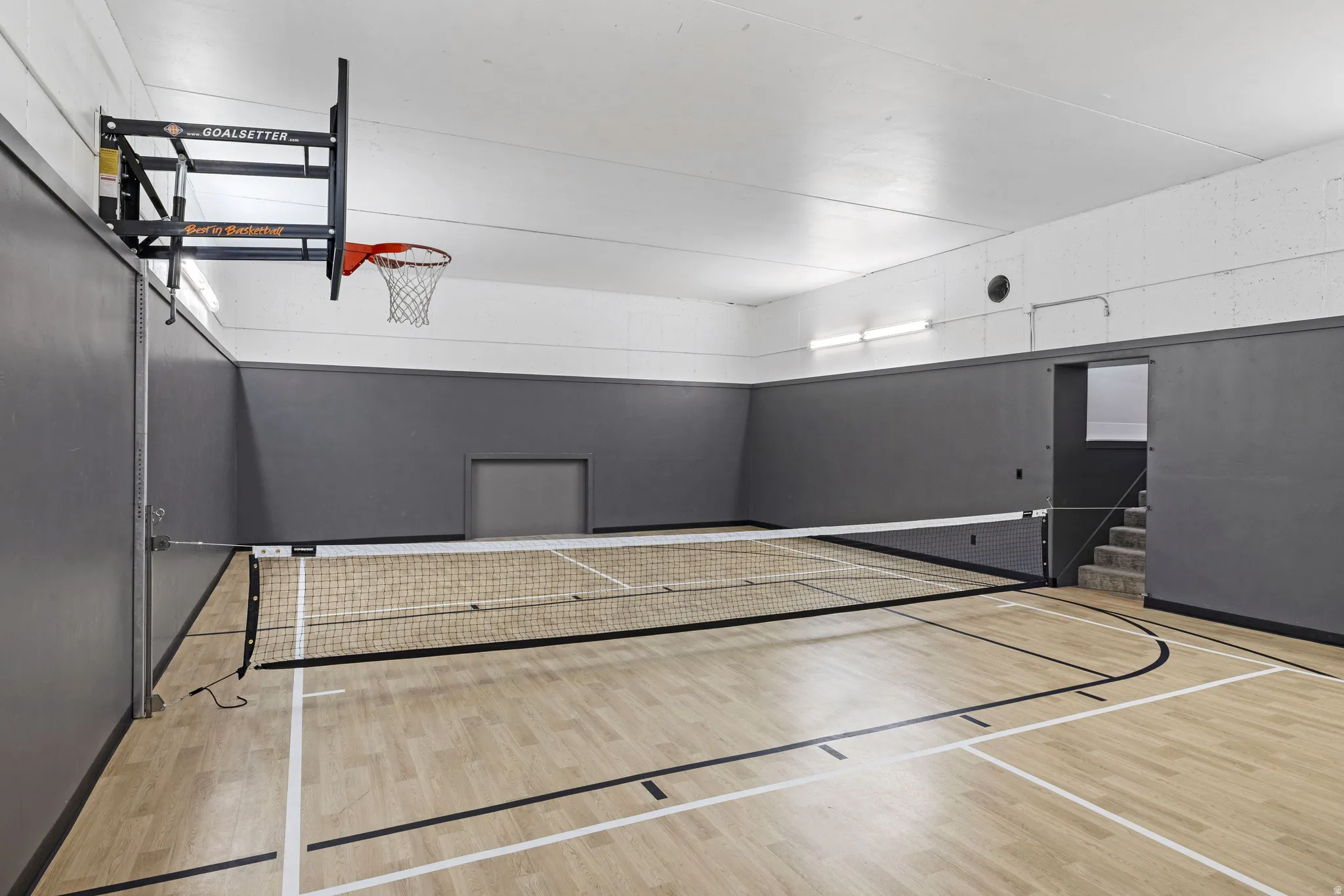 Indoor multi-sport court featuring LVP flooring, a basketball hoop, a pickleball net , and recessed soccer goals.