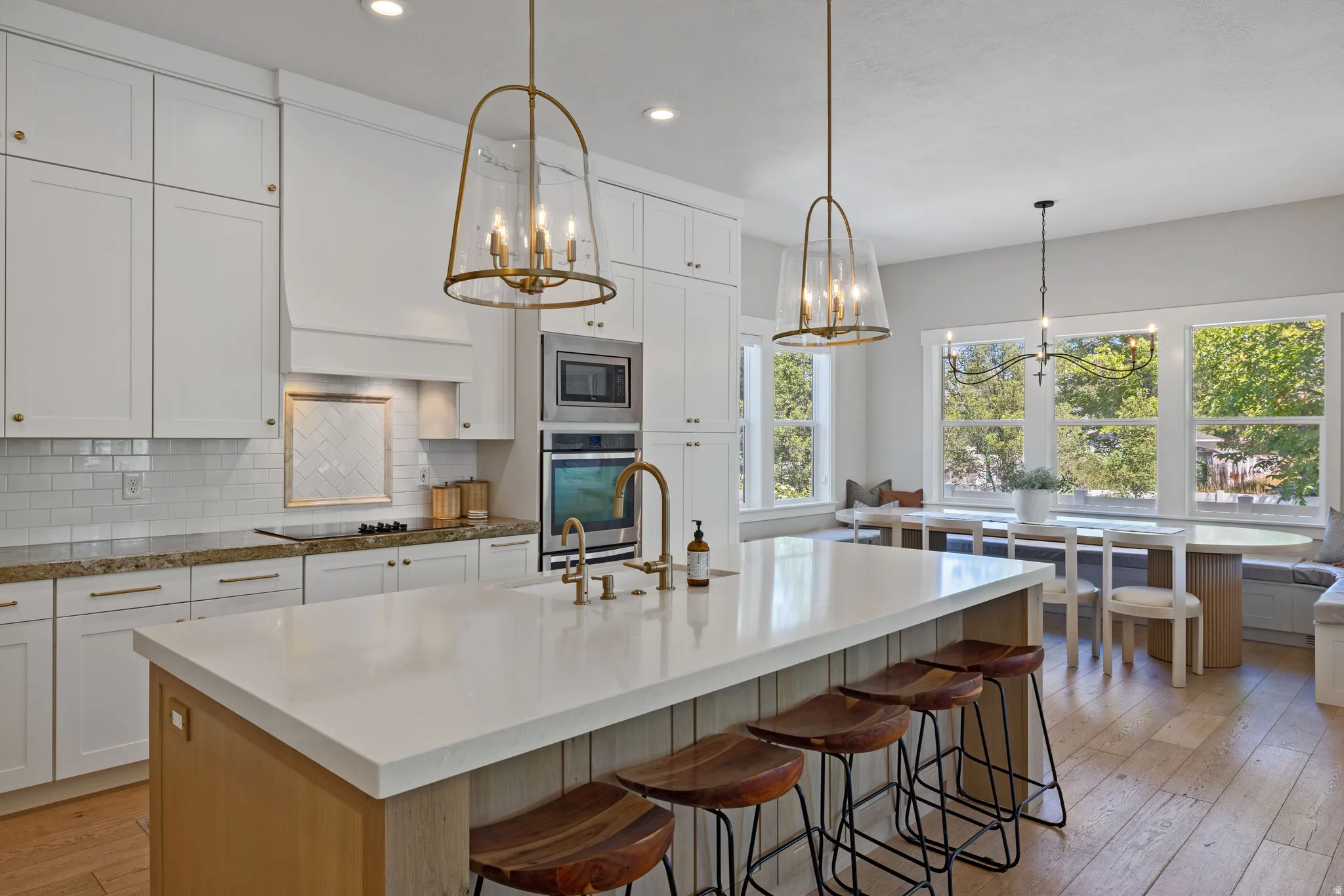 Open-concept kitchen featuring an expansive island with a light-toned countertop, white cabinetry with gold-finish hardware, built-in stainless steel appliances, and wood-finish flooring