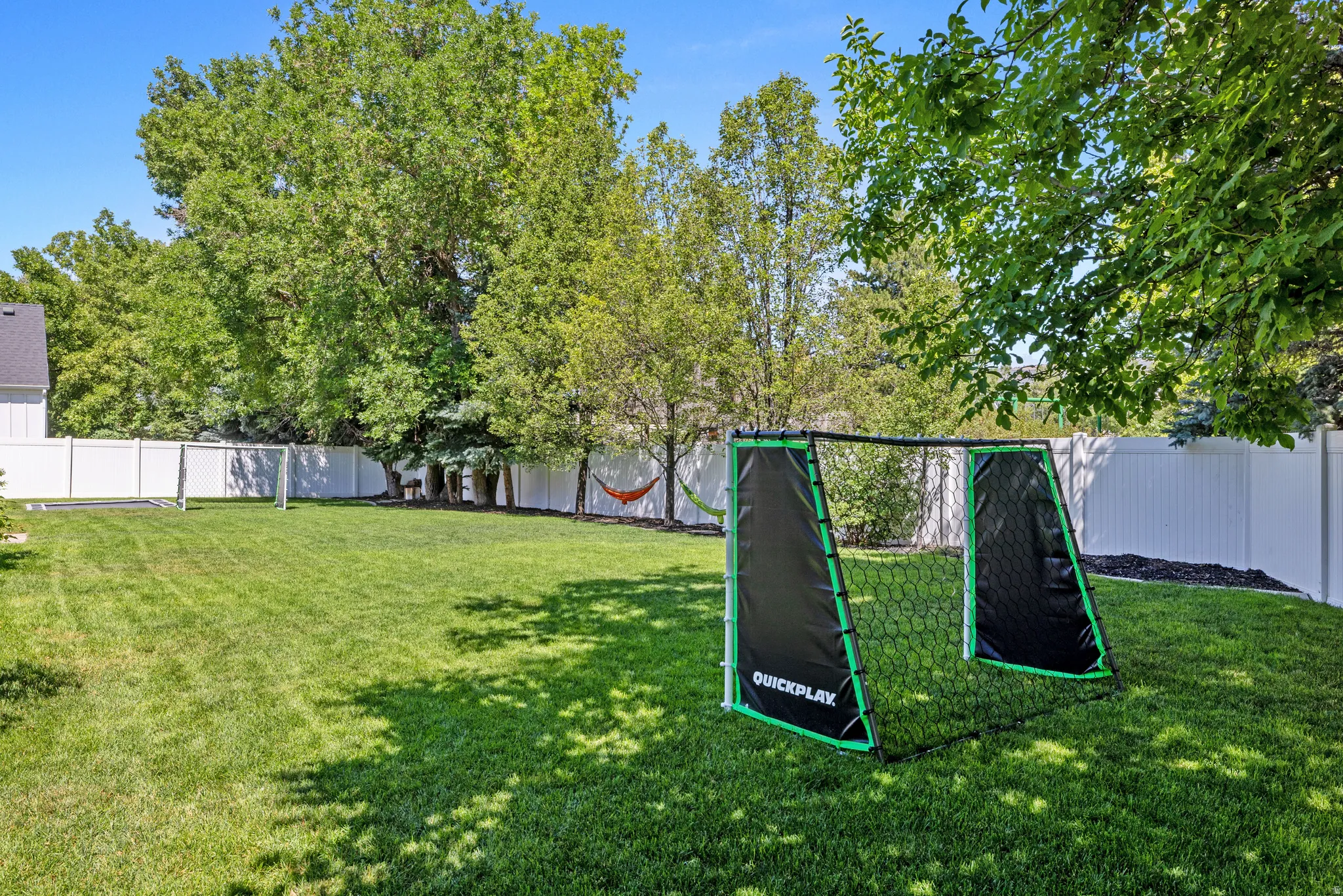 Spacious grassy yard with a white privacy fence, mature trees, and landscaping