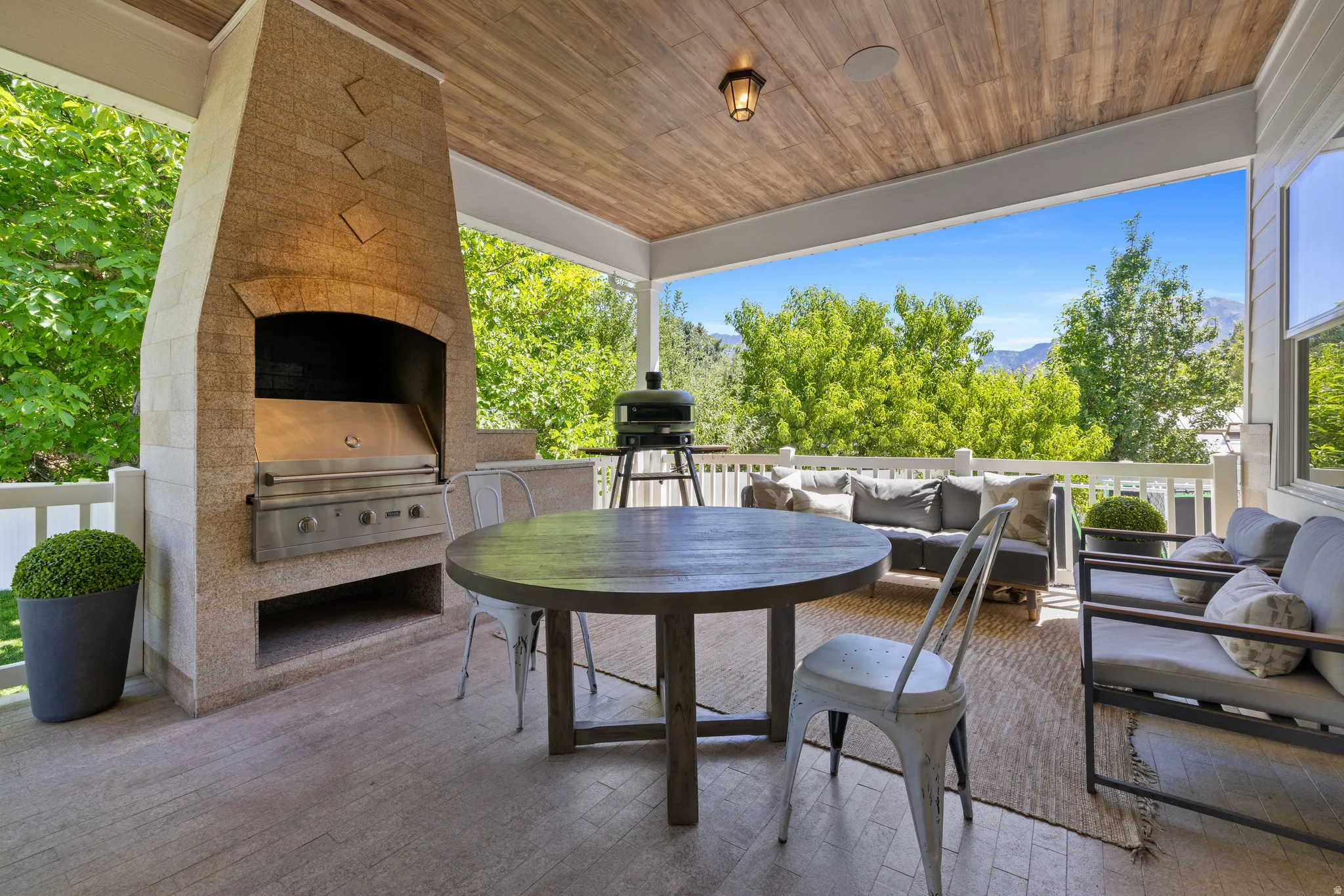 Covered outdoor living space featuring a built-in stone Viking integrated grill, wood-finish ceiling, tile flooring, and white railing