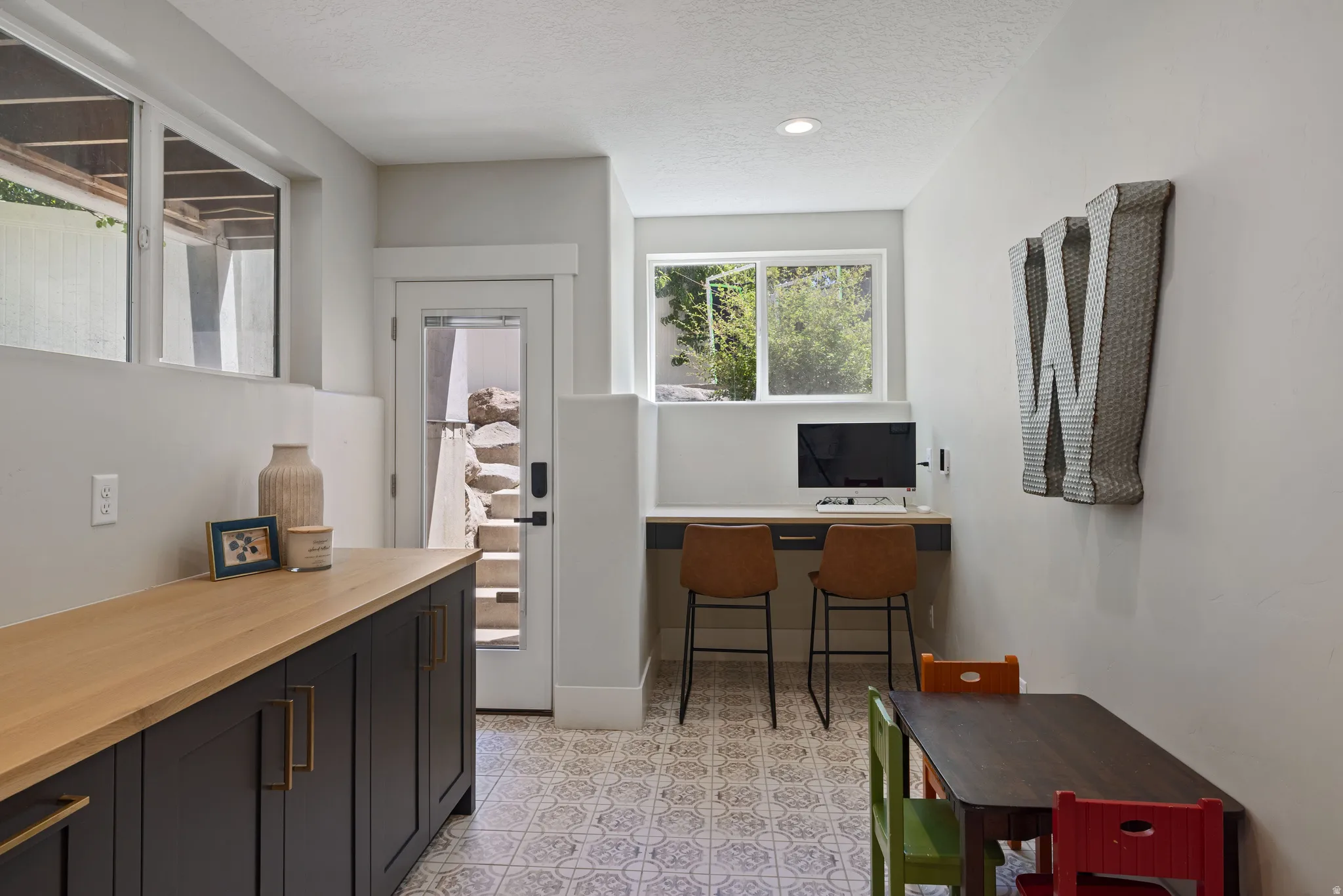 Kitchenette and study room - Versatile lower-level space featuring patterned floor tiles, a built-in desk area  with under-counter storage, and a separate cabinet run with a wood-finish countertop. Basement entrance to the backyard is an added bonus.