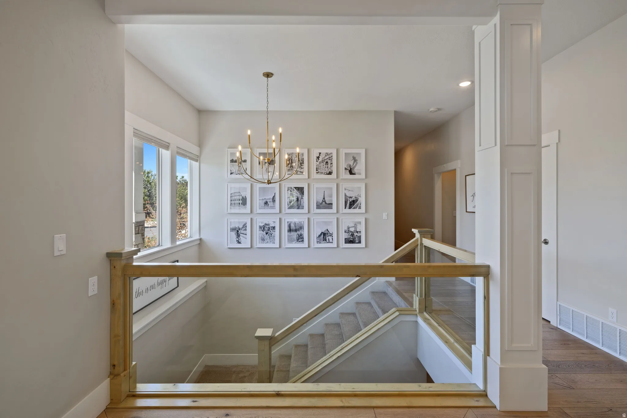 Entry foyer upper landing featuring a contemporary chandelier, large windows with natural light, a wood-finish floor, and a staircase with glass panel railing