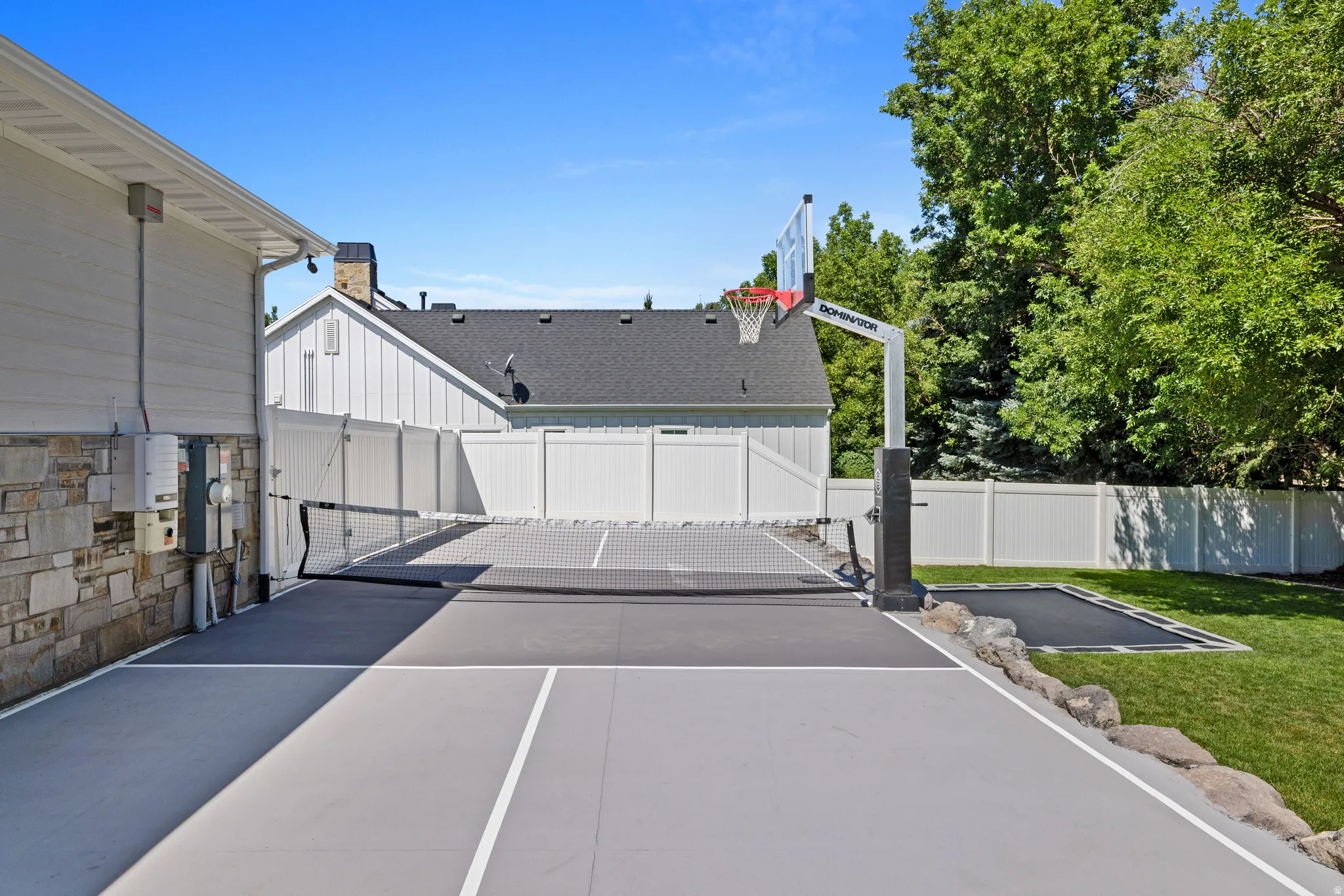 Multi-sport court featuring a basketball hoop and pickleball net, alongside an in-ground trampoline
