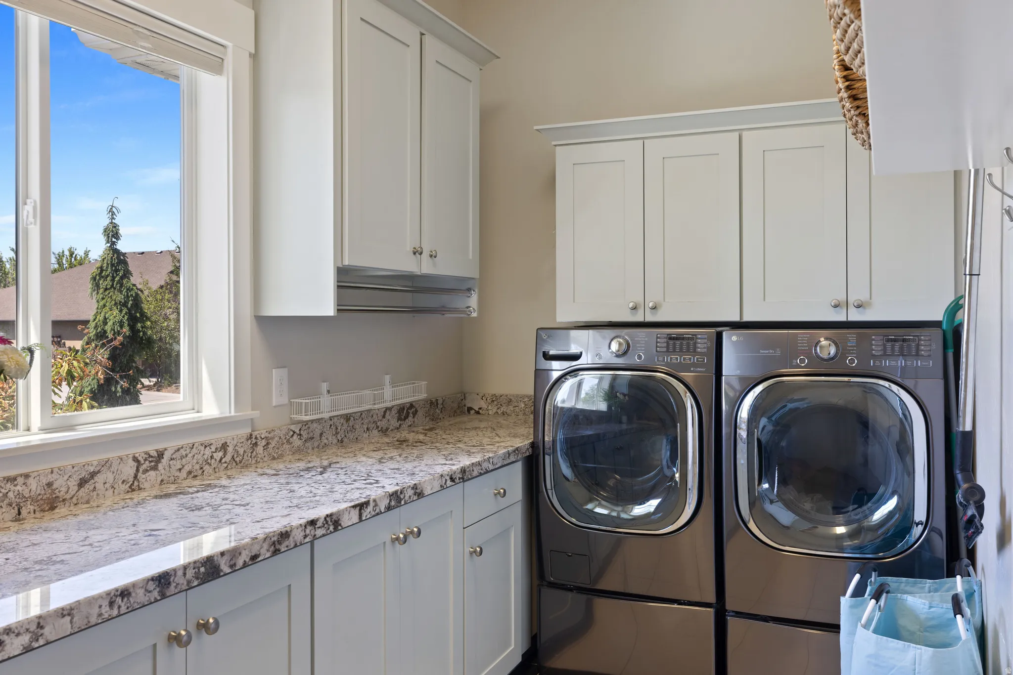 Dedicated laundry space featuring a window, light cabinetry with hardware, extensive countertop, and front-loading appliances