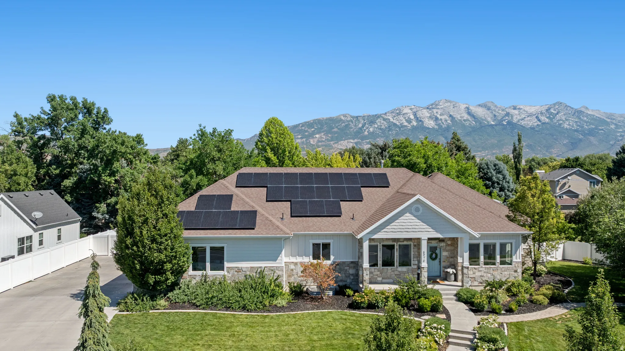 Ranch-style residence featuring solar panels, a stone and siding exterior, a front porch with columns, a curved concrete walkway, and mature landscaping