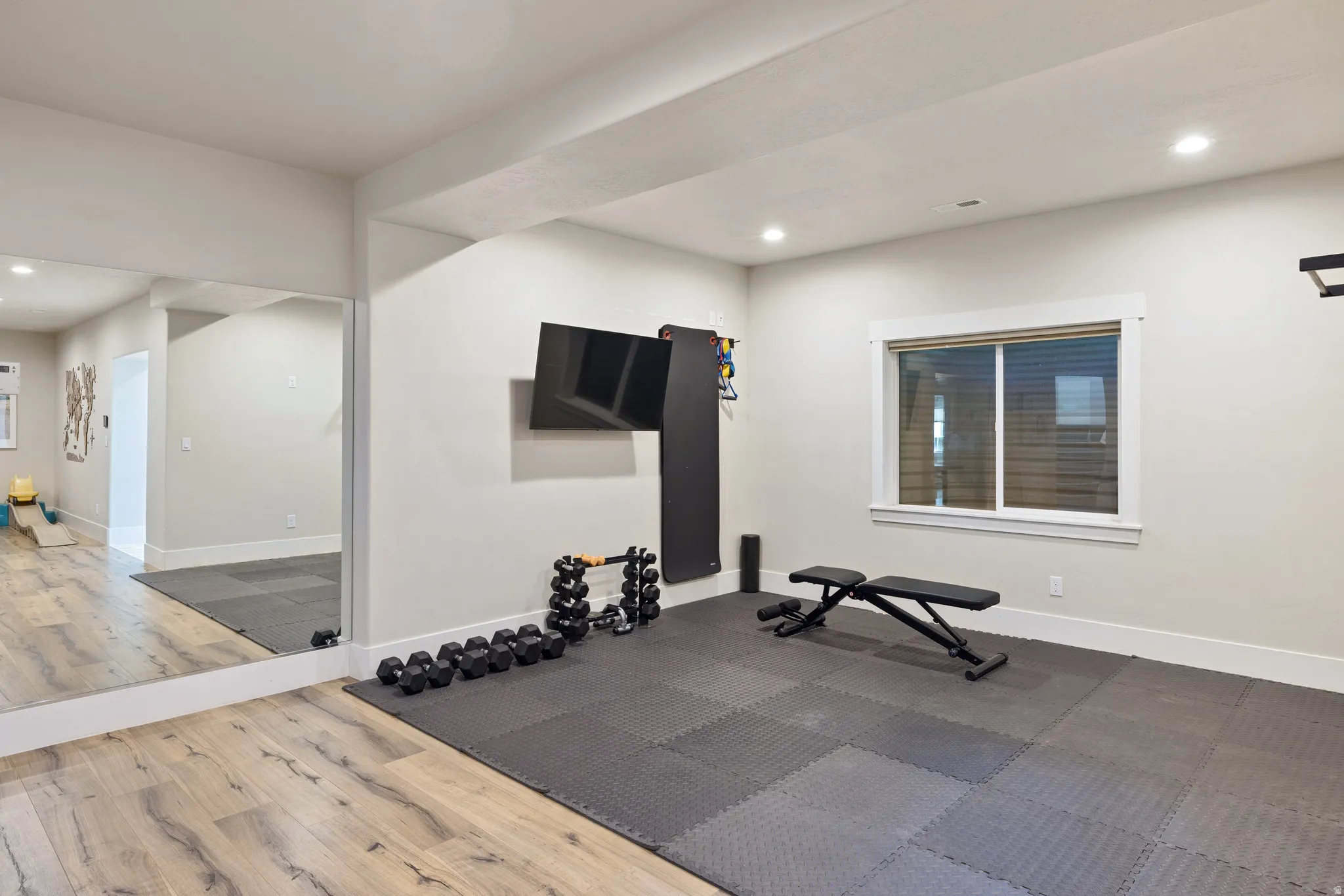 Dedicated gym space featuring recessed lighting, a full-height mirrored wall, and durable rubber mat flooring. Also, a great option for 5th bedroom.