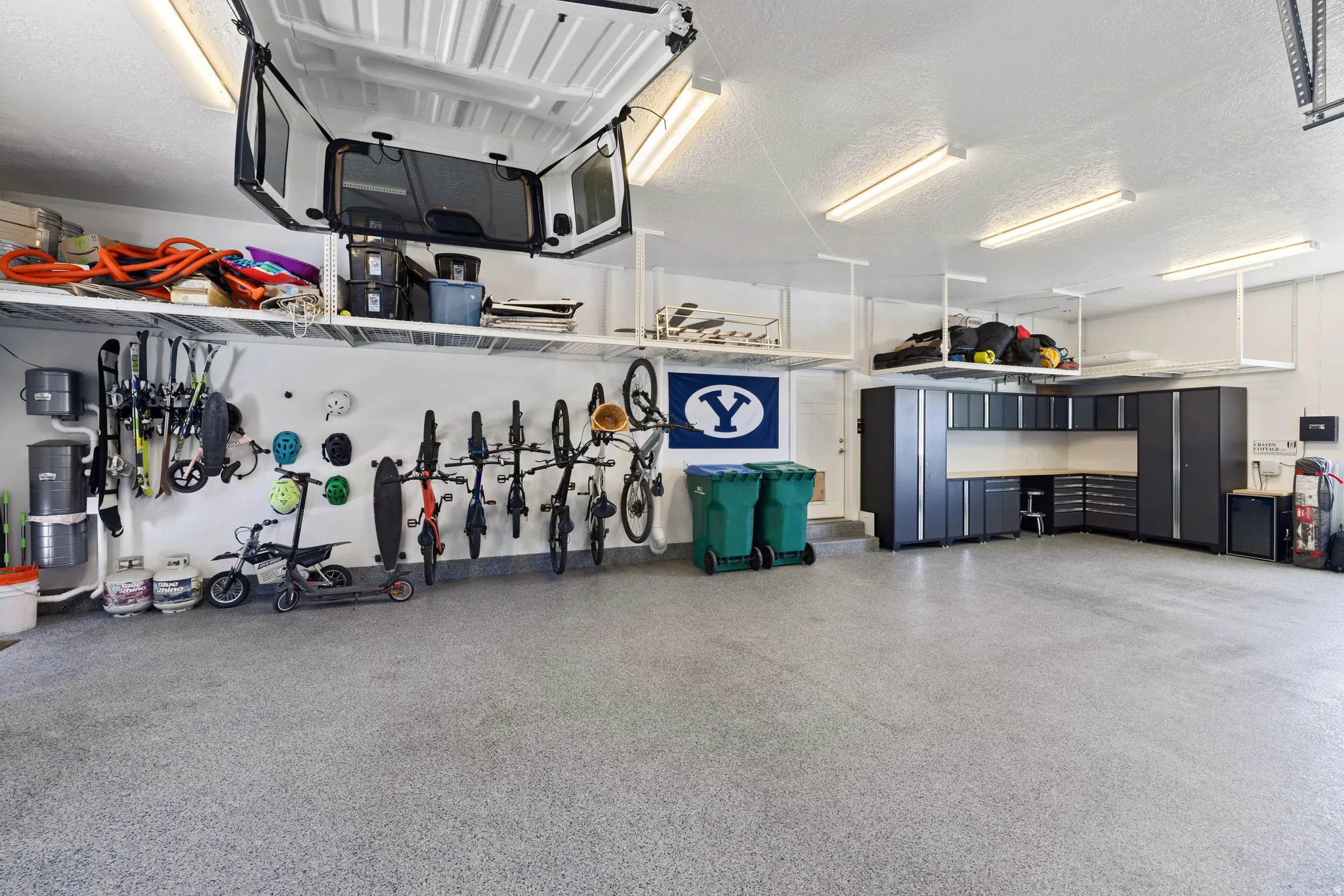 Spacious garage featuring extensive built-in cabinetry with a light-toned countertop, overhead shelving, wall-mounted storage solutions, recessed lighting, and a durable epoxy-coated concrete floor