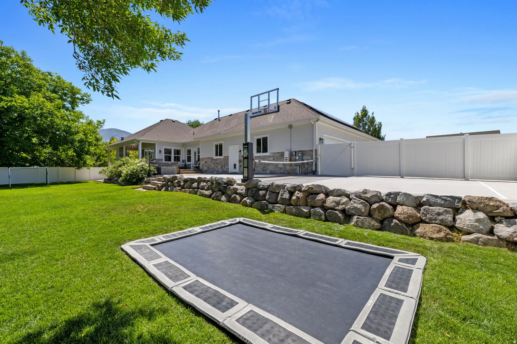 Expansive backyard featuring a lush green lawn, a built-in trampoline, and a large multi-sport court with a basketball hoop
