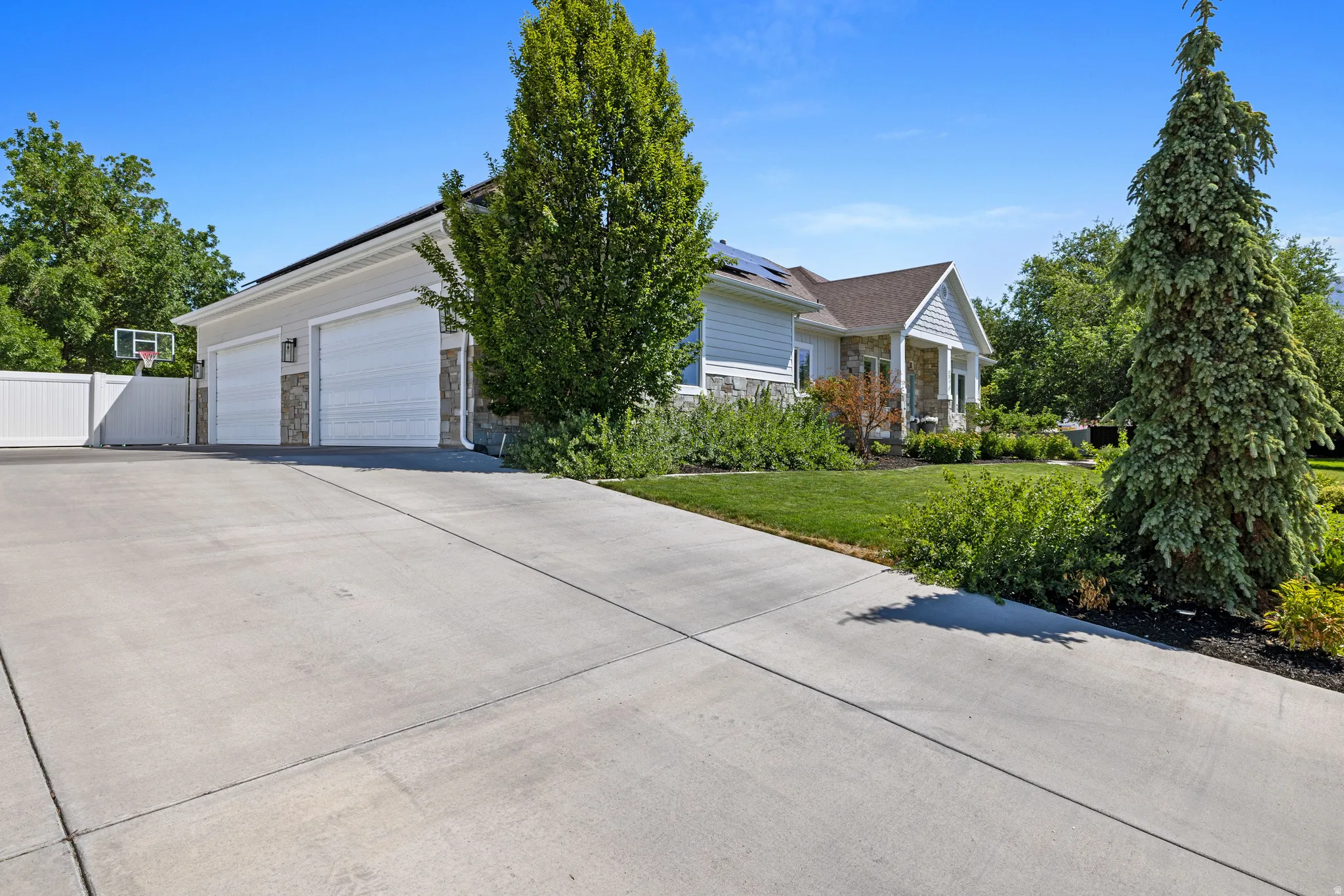Spacious concrete driveway leading to a four-car garage with white paneled doors and stone accents