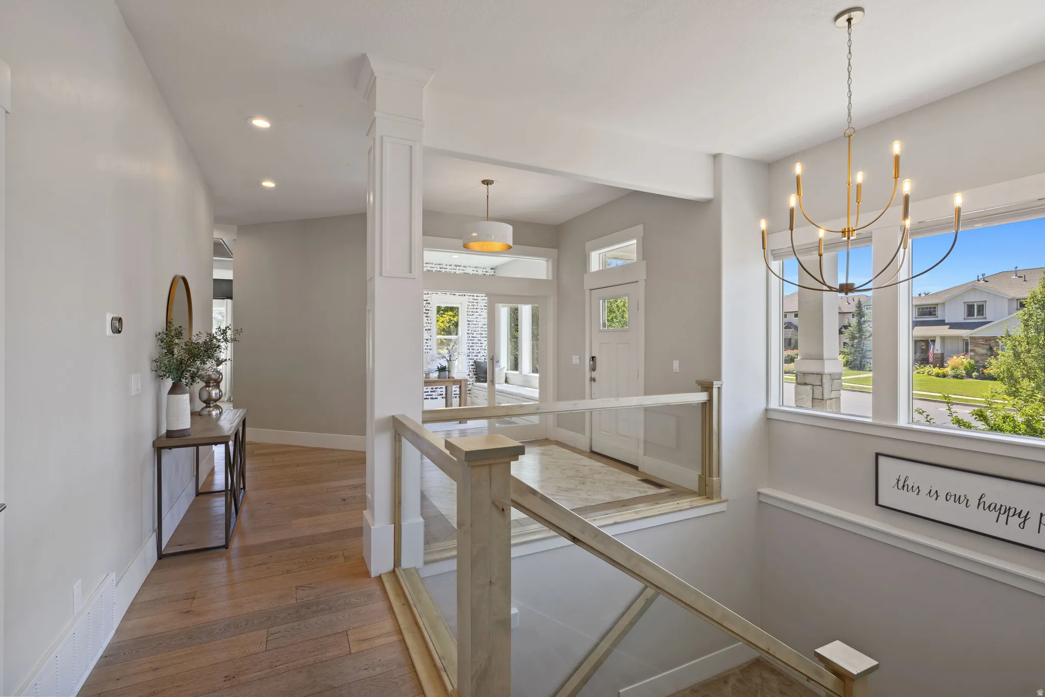 Entry foyer with wood-finish flooring, a modern chandelier, and a glass-paneled staircase featuring a light wood-finish handrail