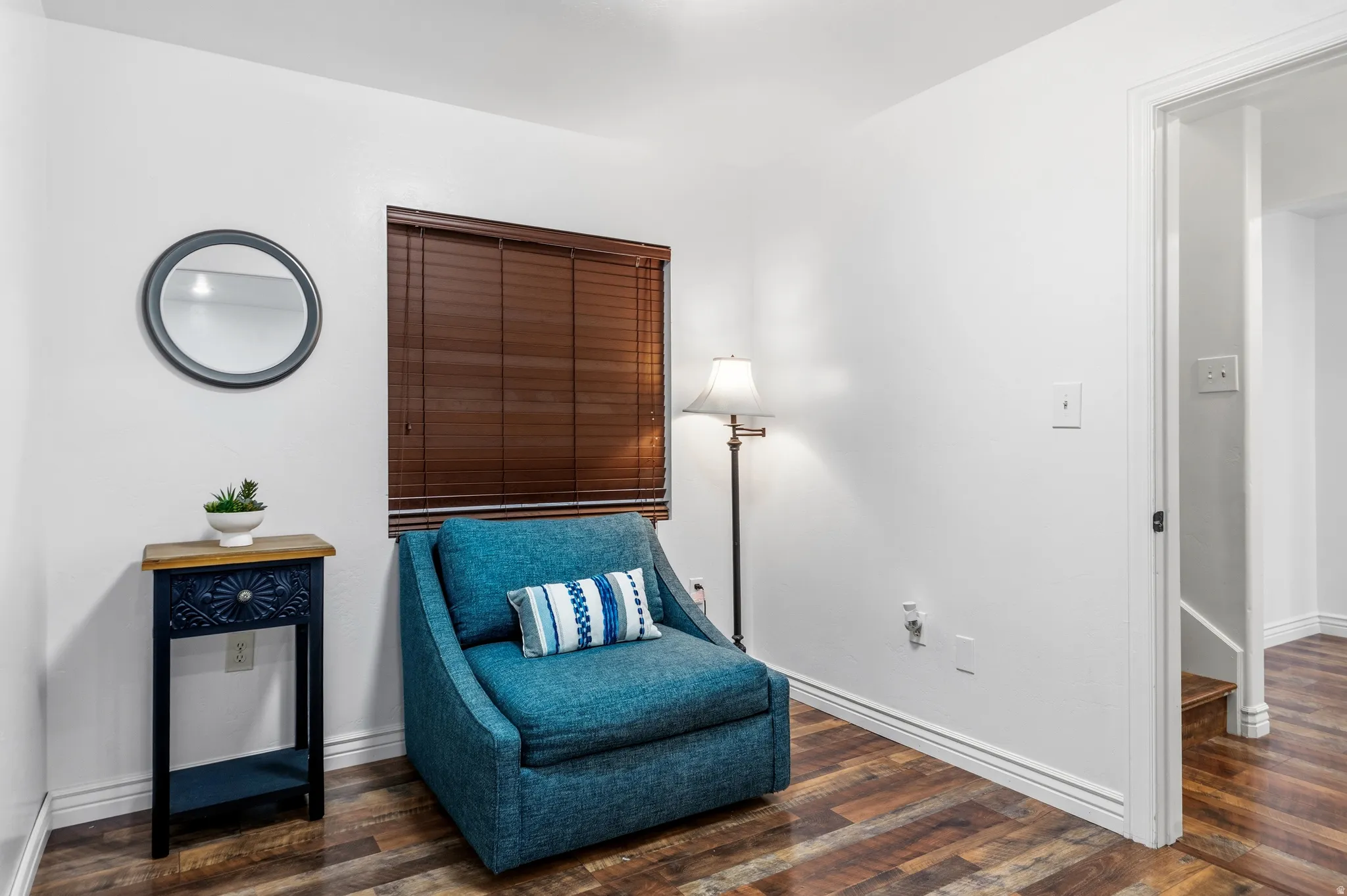 Wood-finish flooring throughout, bright white walls, window with brown blinds, and white trim