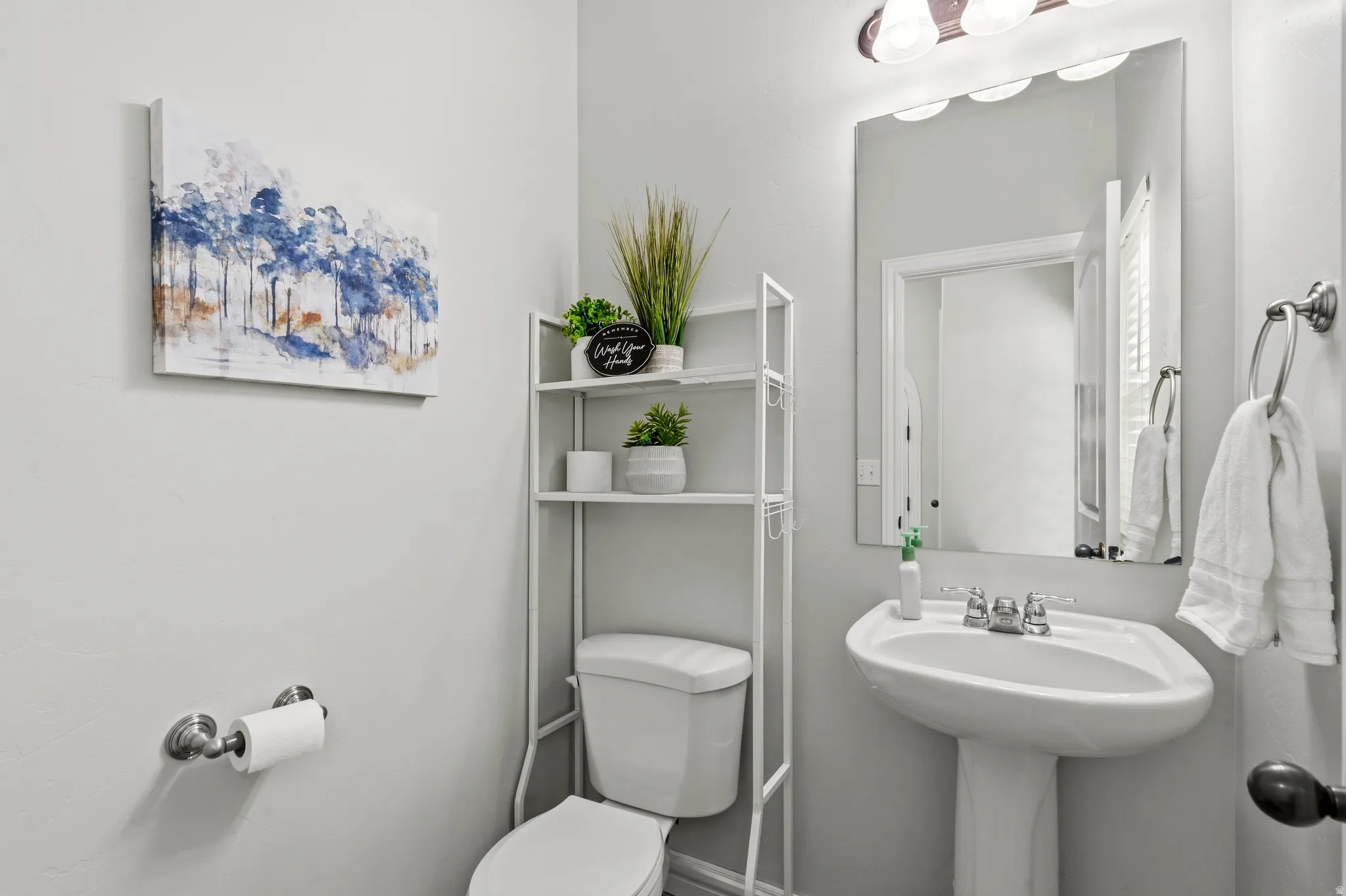 Pedestal sink with chrome-finish faucet, wall-mounted mirror, and vanity light fixture
