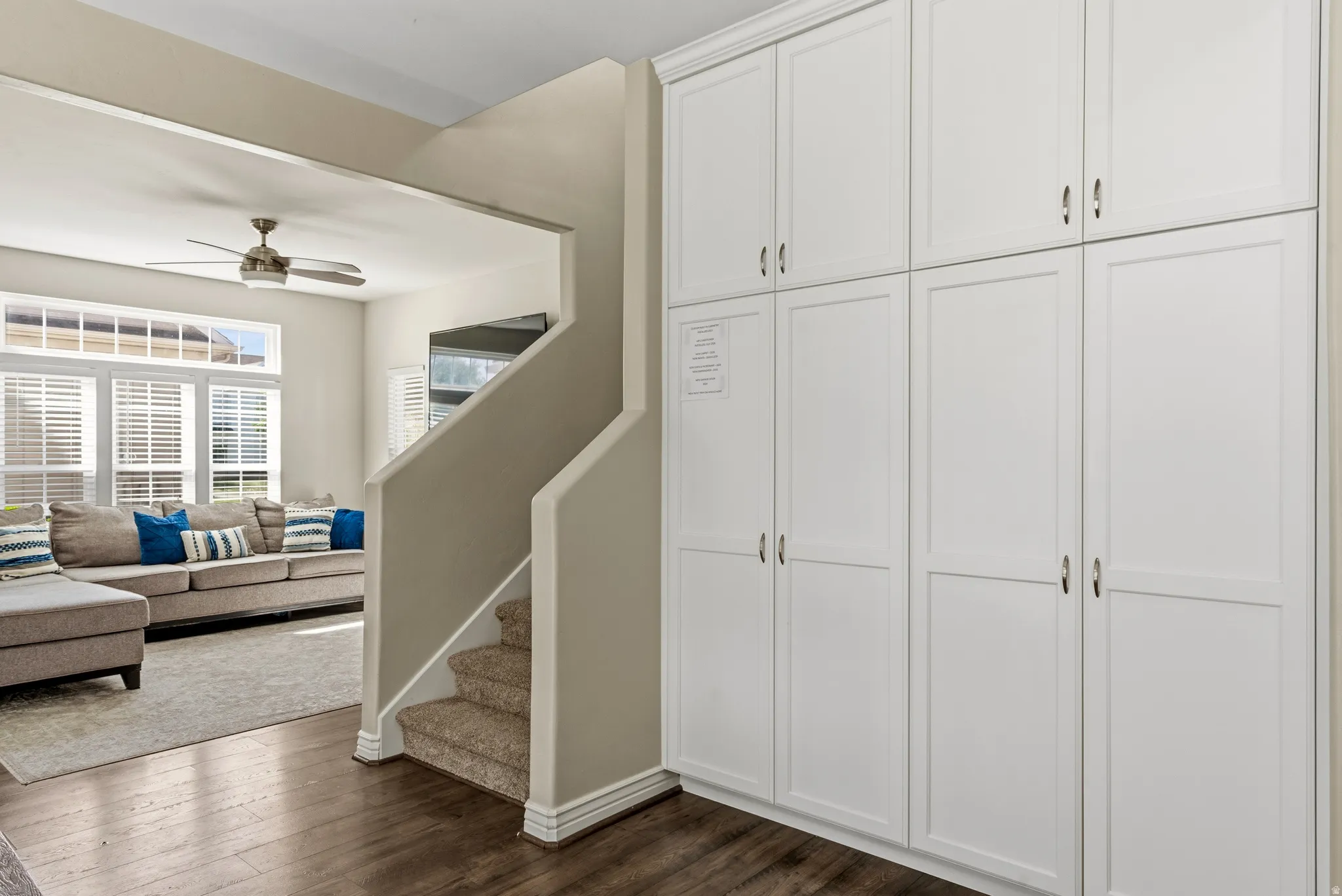 Built-in white paneled cabinetry with metal hardware, wood-finish flooring, and a carpeted staircase
