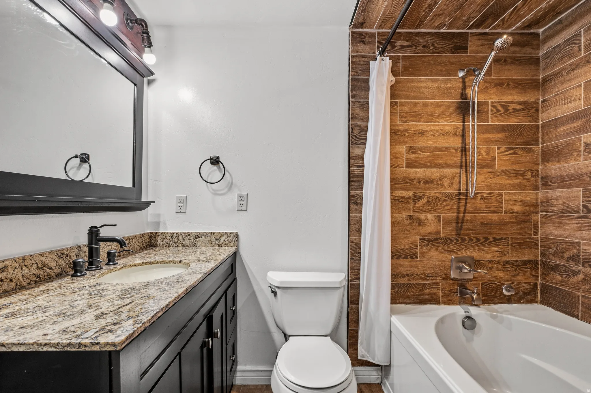 Bathroom featuring a vanity with a granite-style countertop, undermount sink, and dark cabinetry