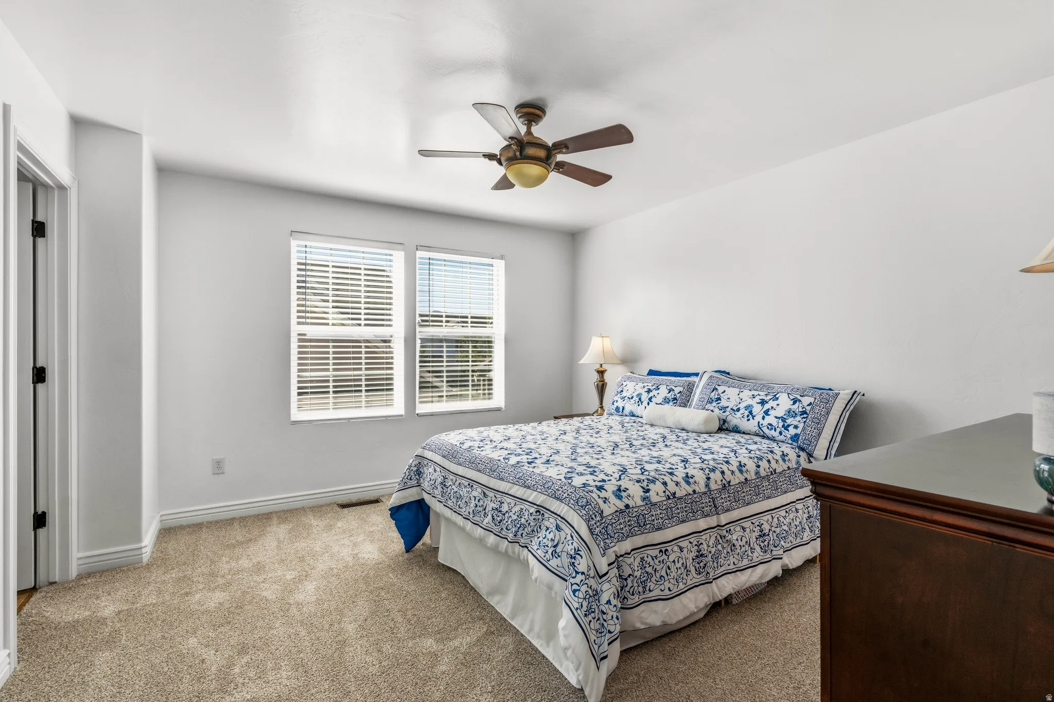 Plush carpeting, two windows with blinds, and an overhead ceiling fan