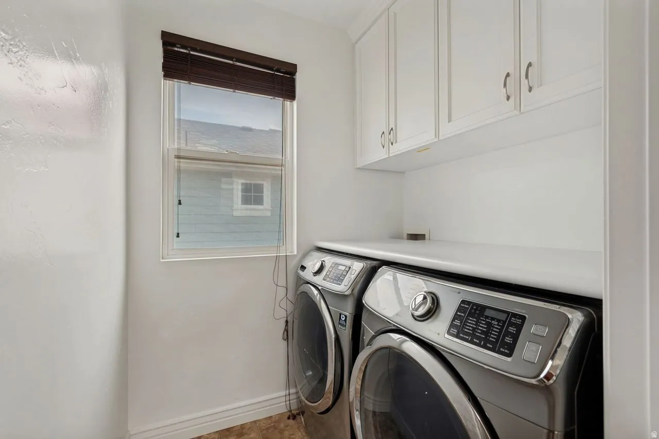 Dedicated laundry area featuring white upper cabinetry, a window with wood blinds, and a built-in countertop above appliances