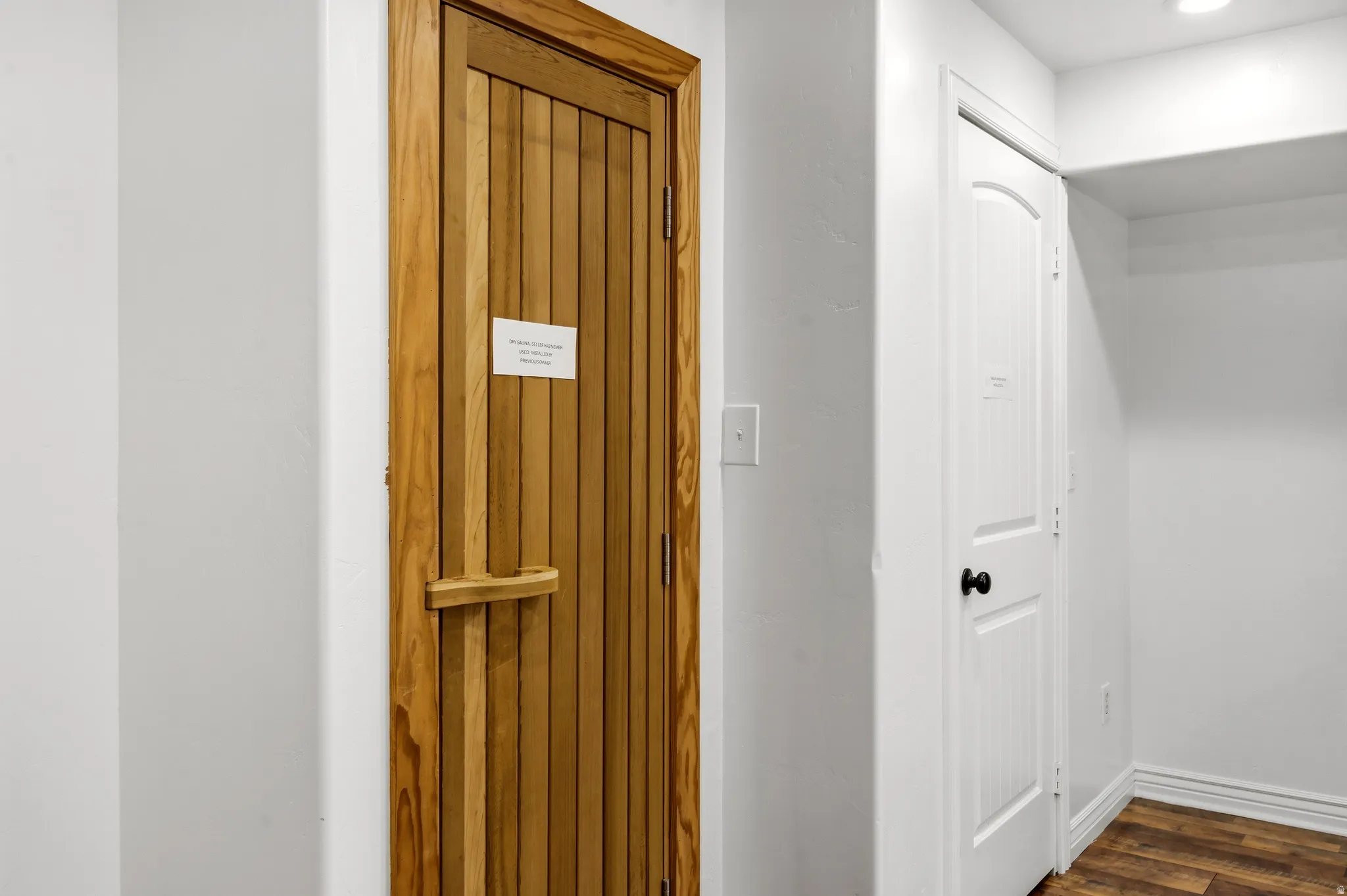 Wood-paneled door with a matching horizontal handle, white interior doors, and wood-finish flooring