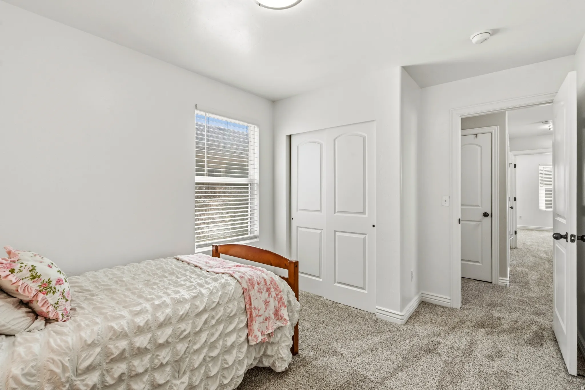 Bright secondary bedroom featuring neutral carpeting, a large double-hung window with plantation shutters, and a wood-frame bed frame