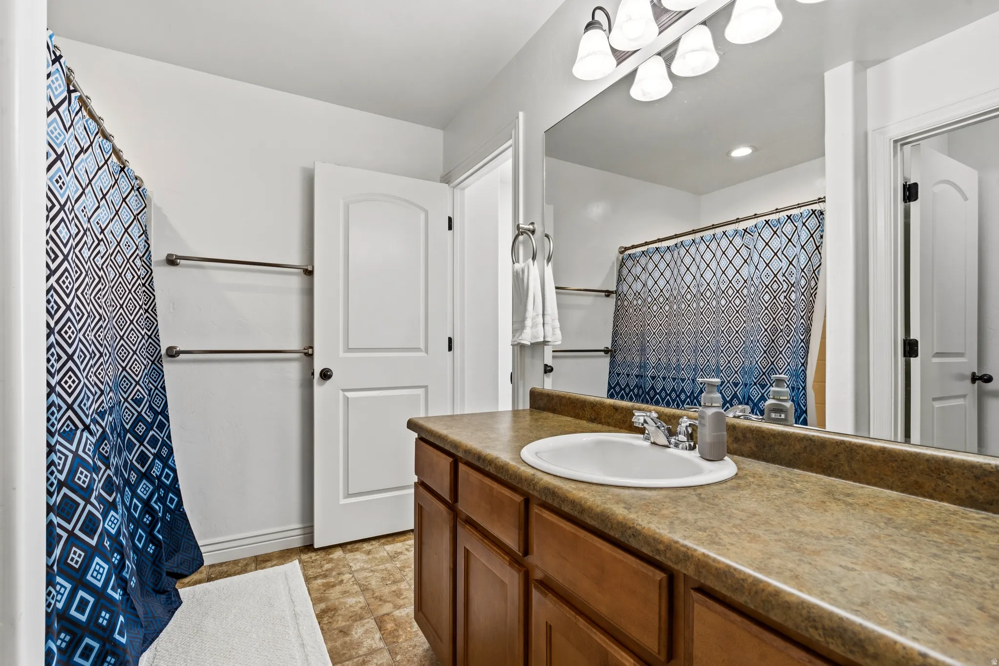 Vanity with an integrated sink, expansive countertop, wood-finish cabinetry, and overhead lighting