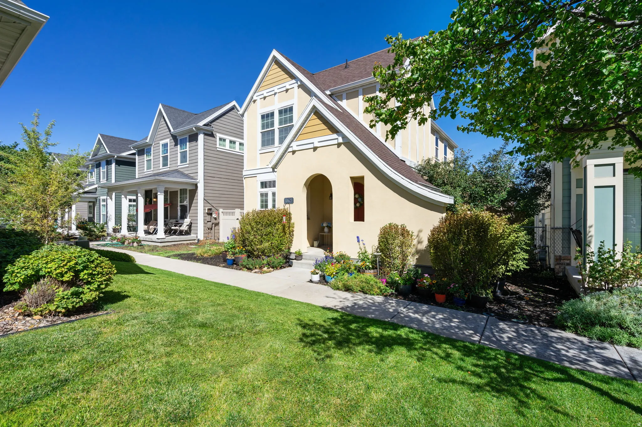 Stucco and siding exterior, arched entry, gabled rooflines, mature landscaping, and concrete walkways