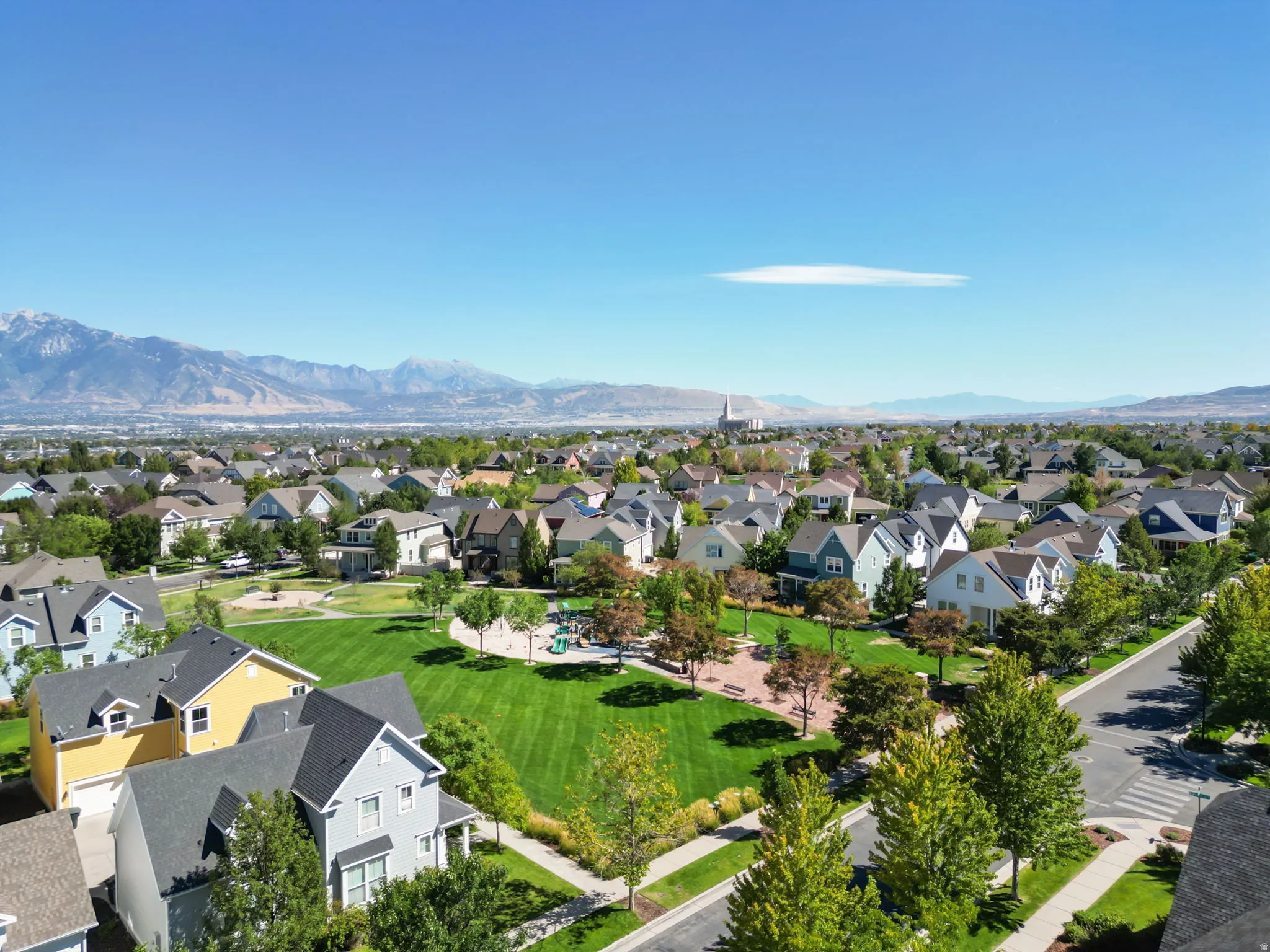 Mountain backdrop, neighborhood green space, paved walkways, mature trees, residential street