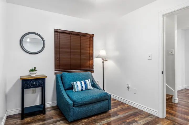 Wood-finish flooring throughout, bright white walls, window with brown blinds, and white trim