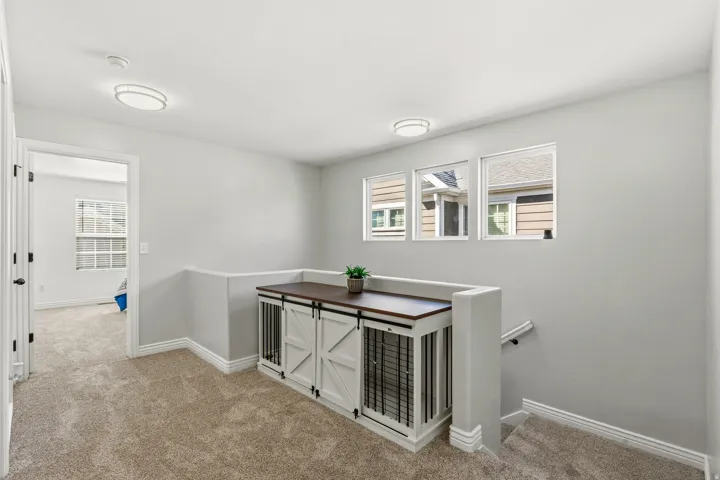 Plush carpet flooring, three clear-pane windows, recessed lighting, and a built-in cabinet with a wood-finish countertop