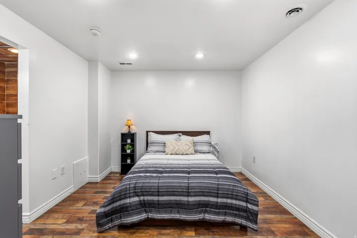 Bright secondary bedroom featuring recessed ceiling lighting, white walls, and warm wood-finish flooring
