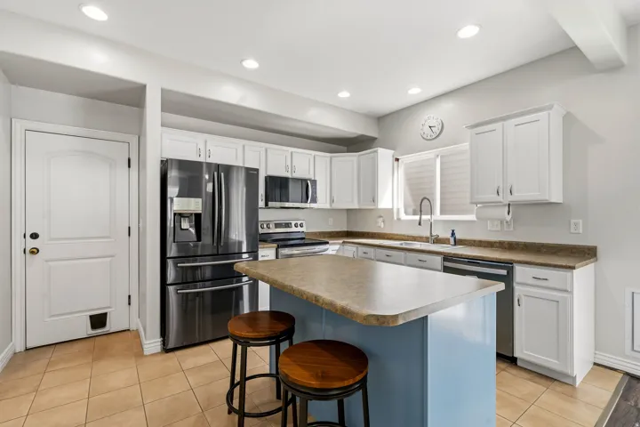 Kitchen featuring white cabinetry, stainless steel appliances, an island with countertop seating, and recessed lighting