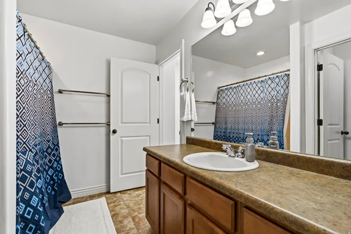 Vanity with an integrated sink, expansive countertop, wood-finish cabinetry, and overhead lighting